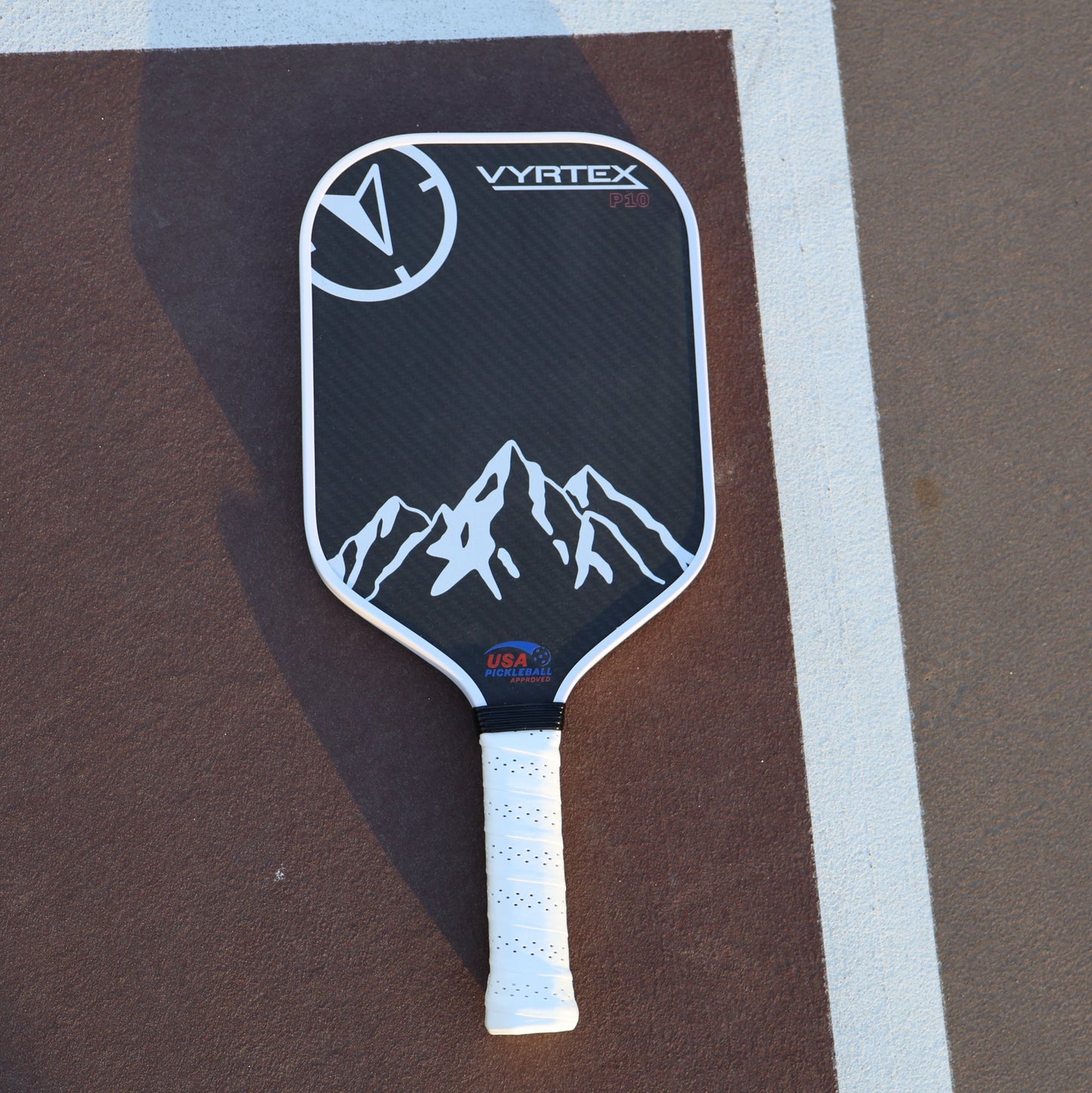 Vyrtex Carbon FIber paddle lying on a pickleball court at sunset